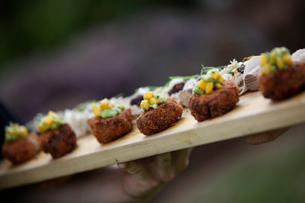 Server holding a wooden board of passed canapes topped with mango salsa