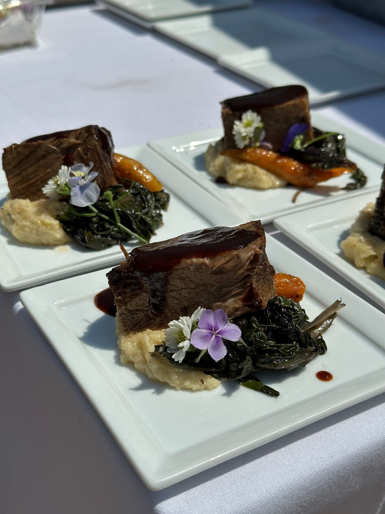 Plated short rib over polenta with seasonal vegetables and edible flowers