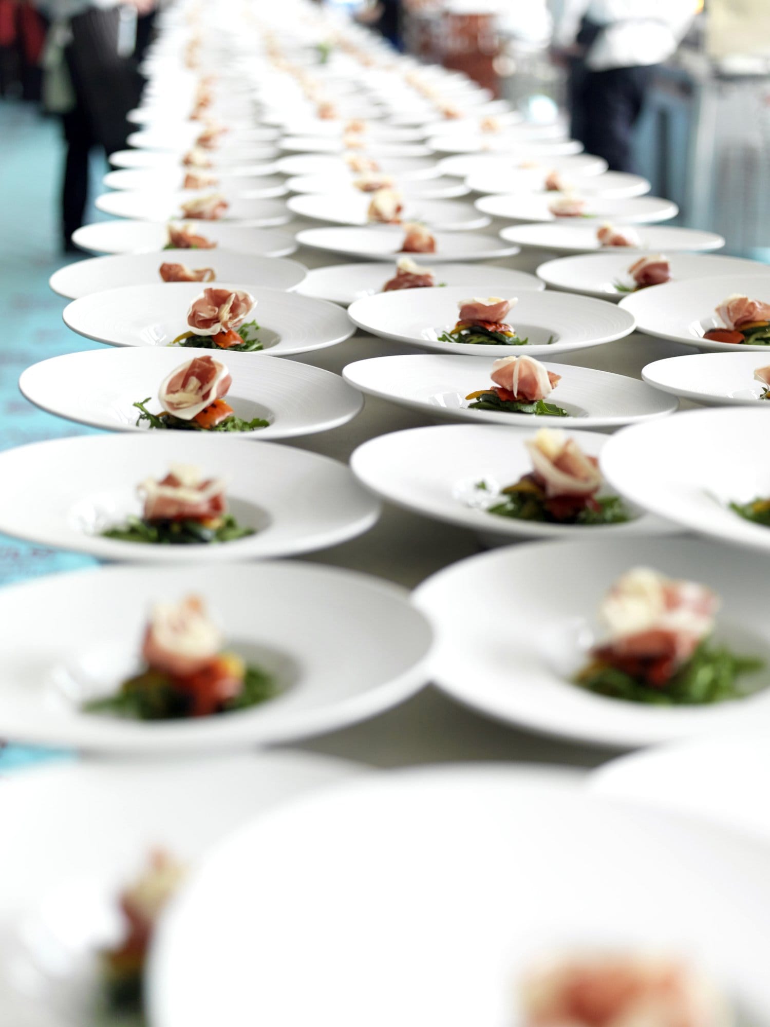 Long banquet table lined with rows of plated prosciutto-and-arugula appetizers