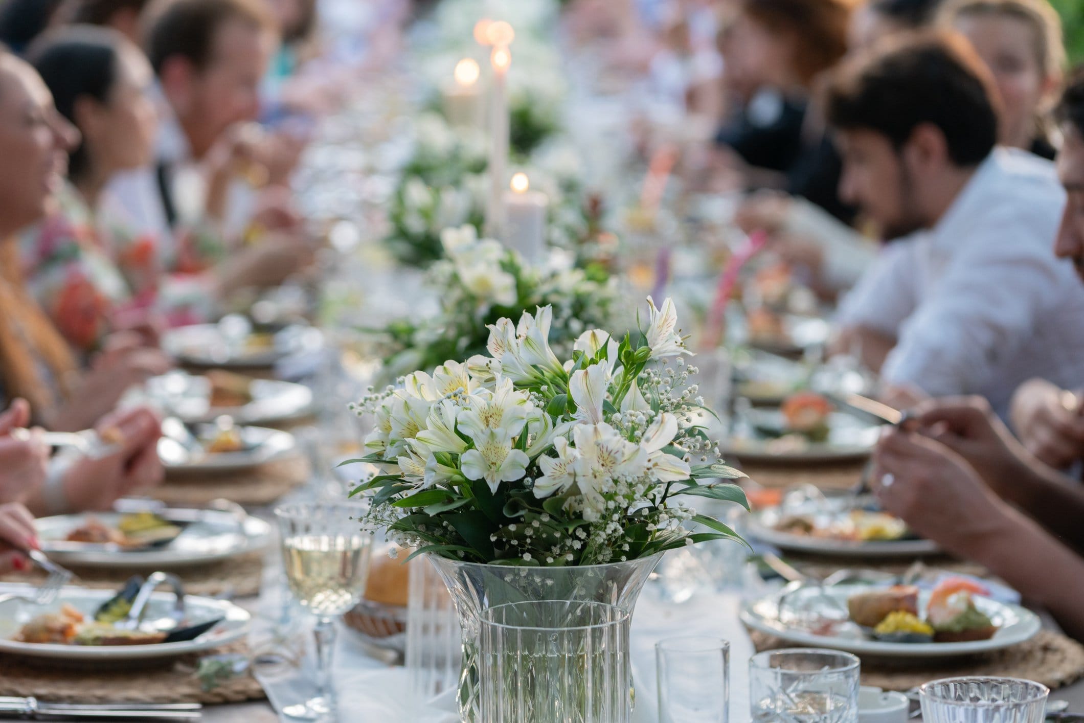 Guests dining at a long banquet table with floral centerpieces and candles