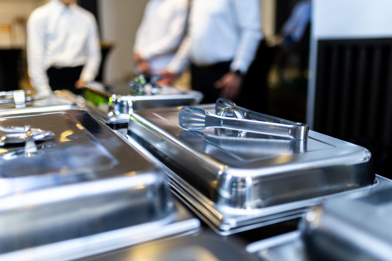 Stainless chafing dishes stacked for buffet service with catering staff behind