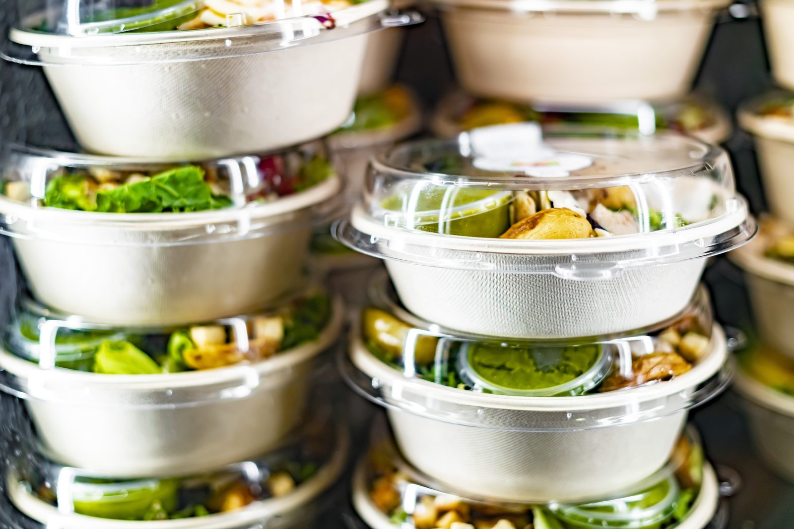 Stacked grab-and-go meal boxes, each with salad, toppings, and a sealed dressing pot