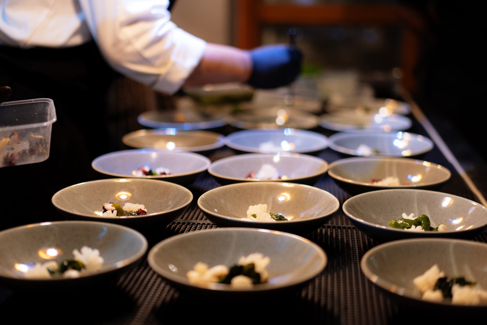 Chef plating garnished bowls in long rows during low-light service