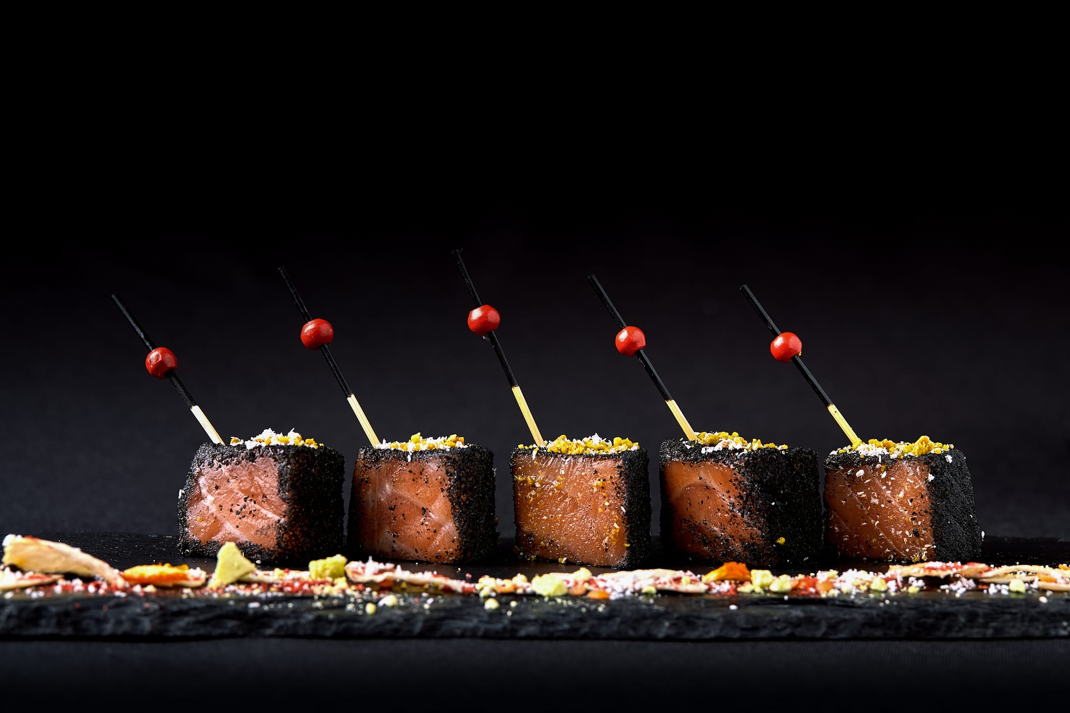 Black sesame-crusted seared tuna bites on cocktail picks, plated on dark slate